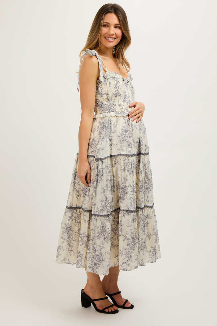 woman wearing a cream floral print maternity tiered maxi dress with ruffled straps and a visible baby bump