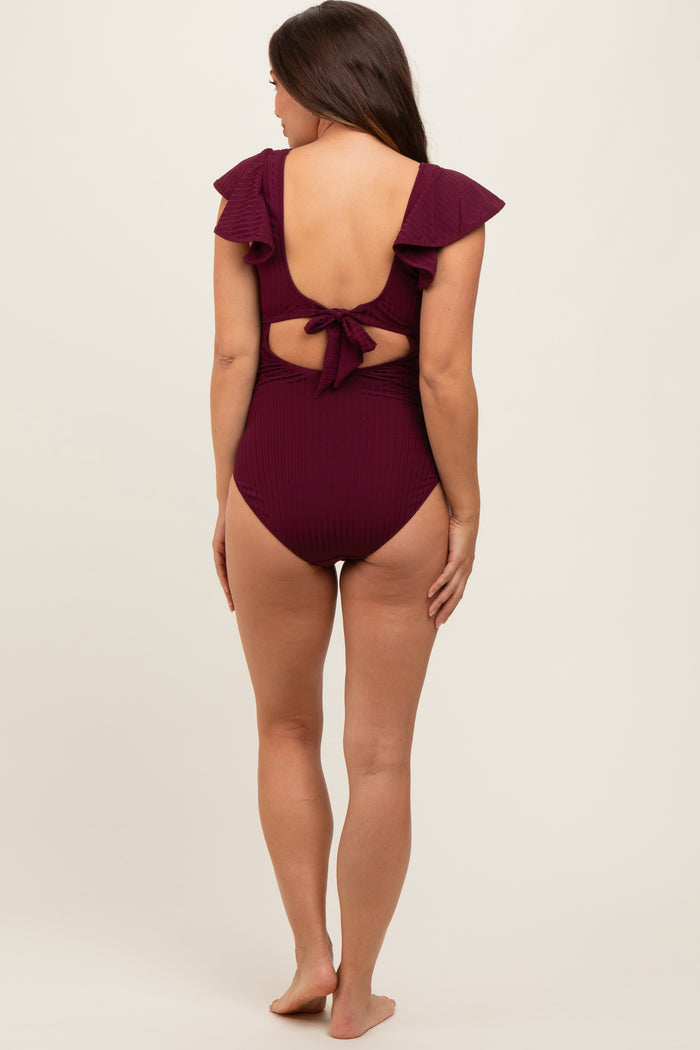 woman wearing a maroon maternity one-piece swimsuit with ruffle details and a tied back, showcasing a baby bump