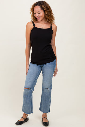 woman wearing a black ribbed tank top and light wash ripped jeans with black flats, standing and smiling