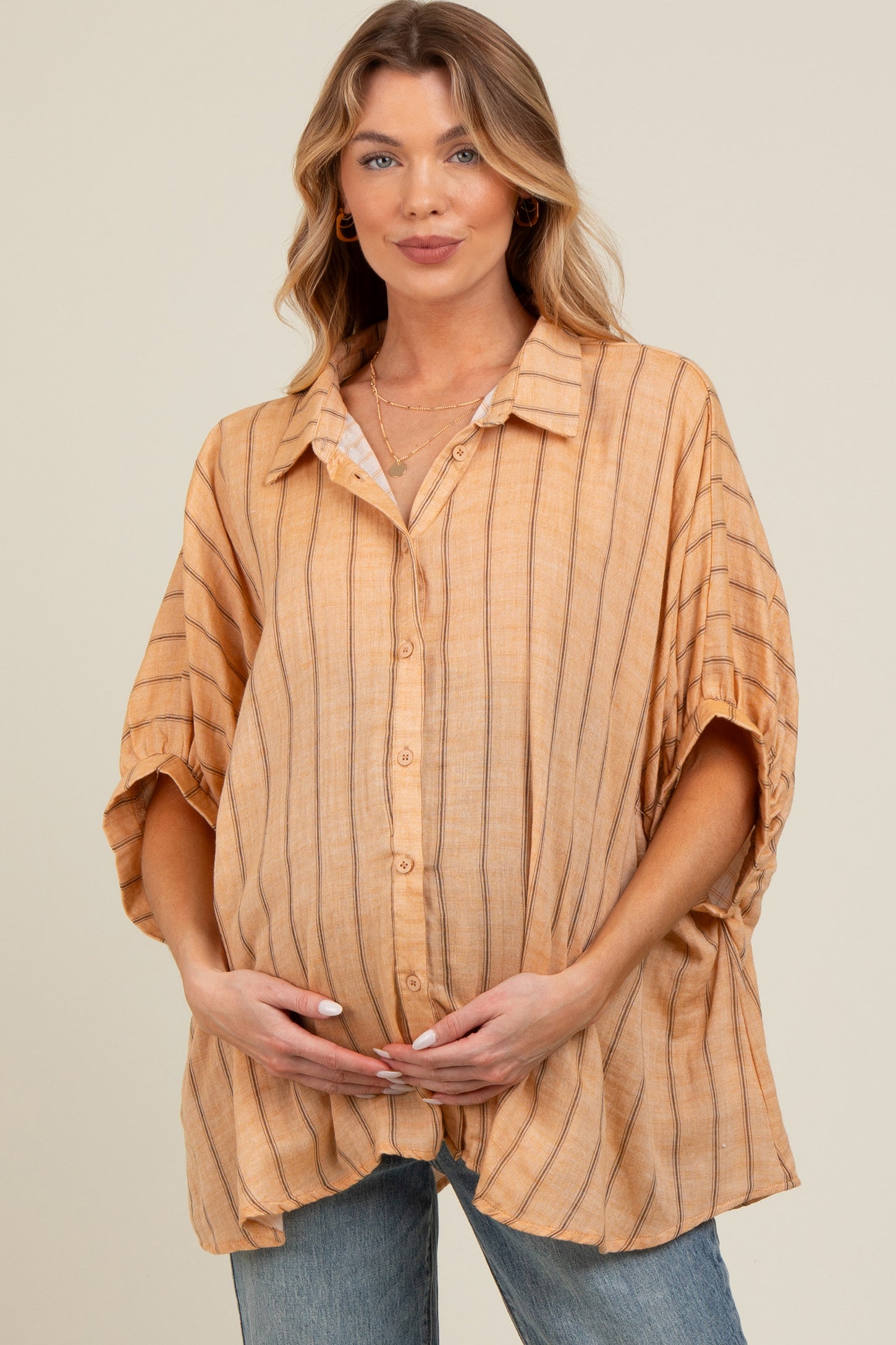 woman wearing a striped peach maternity button-up shirt and holding her baby bump