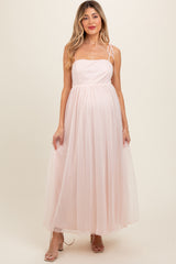 woman wearing a blush pink maternity gown with a fitted bodice and flowy tulle skirt, showing her baby bump