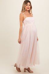 woman wearing a light pink maternity maxi dress with spaghetti straps and a flowing tulle skirt, showcasing her baby bump