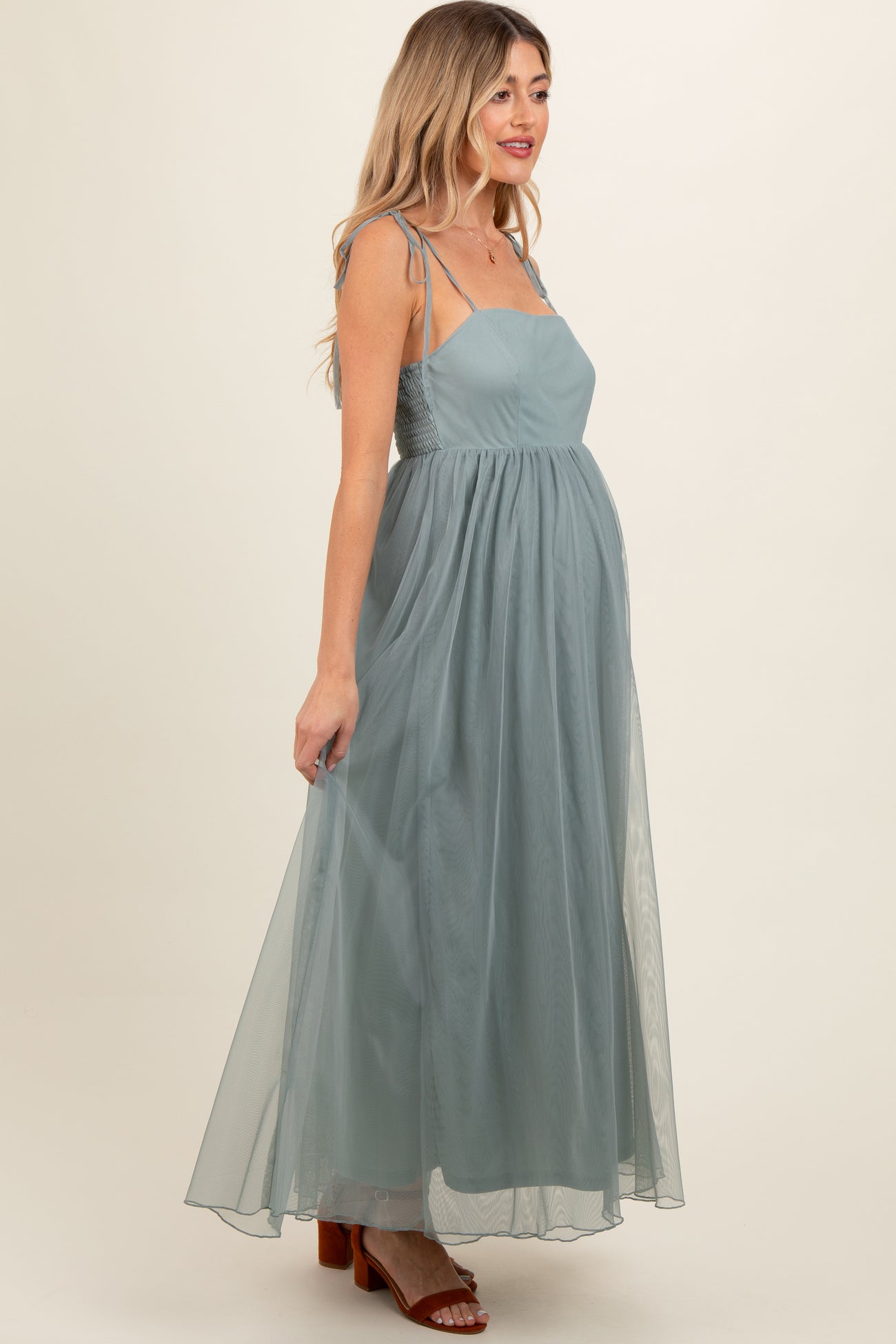 woman wearing a flowing light teal maternity maxi dress with adjustable straps and a fitted bodice, showing her baby bump