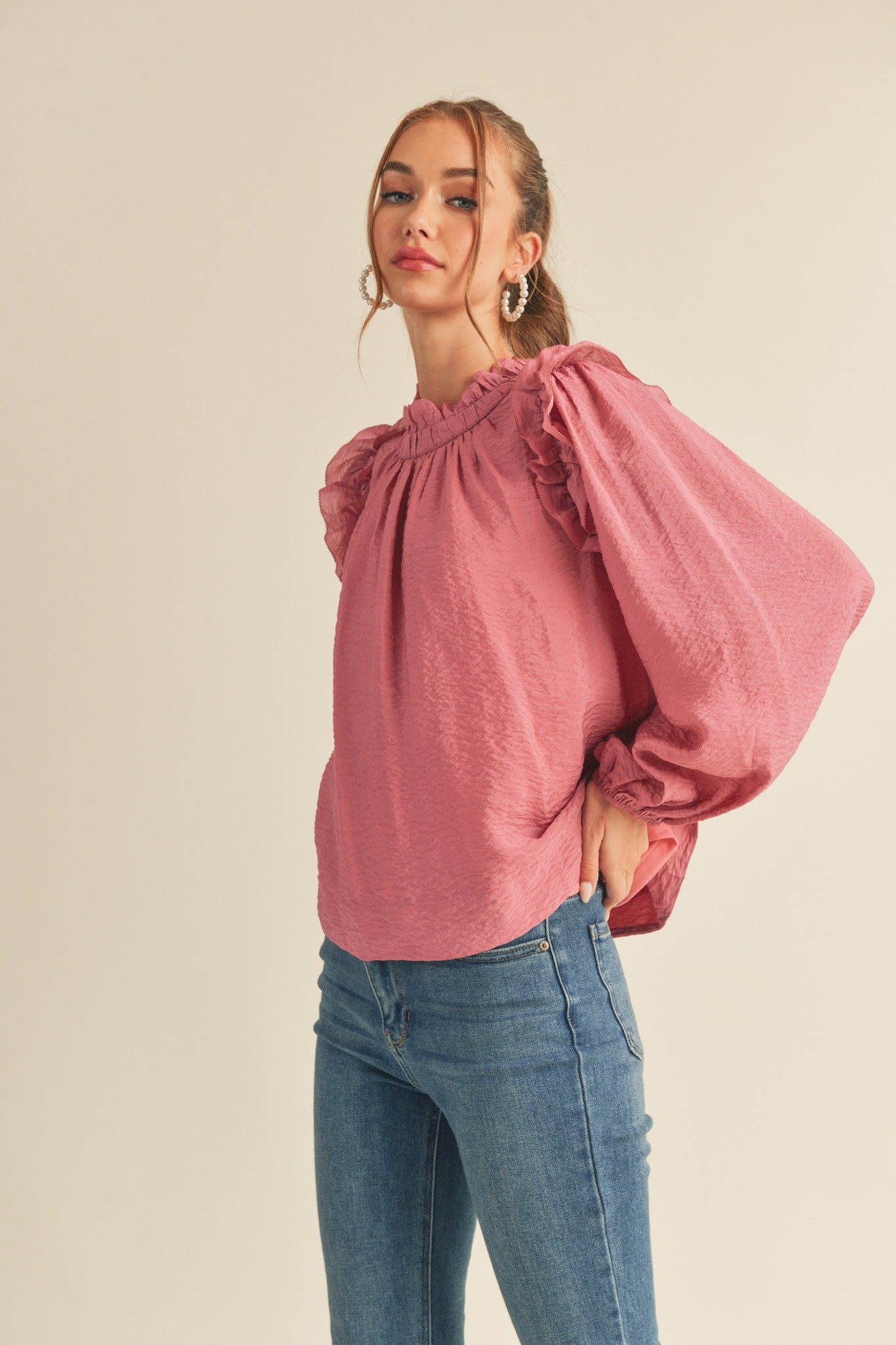 woman wearing a pink textured blouse with a ruffled neckline and balloon sleeves paired with blue jeans