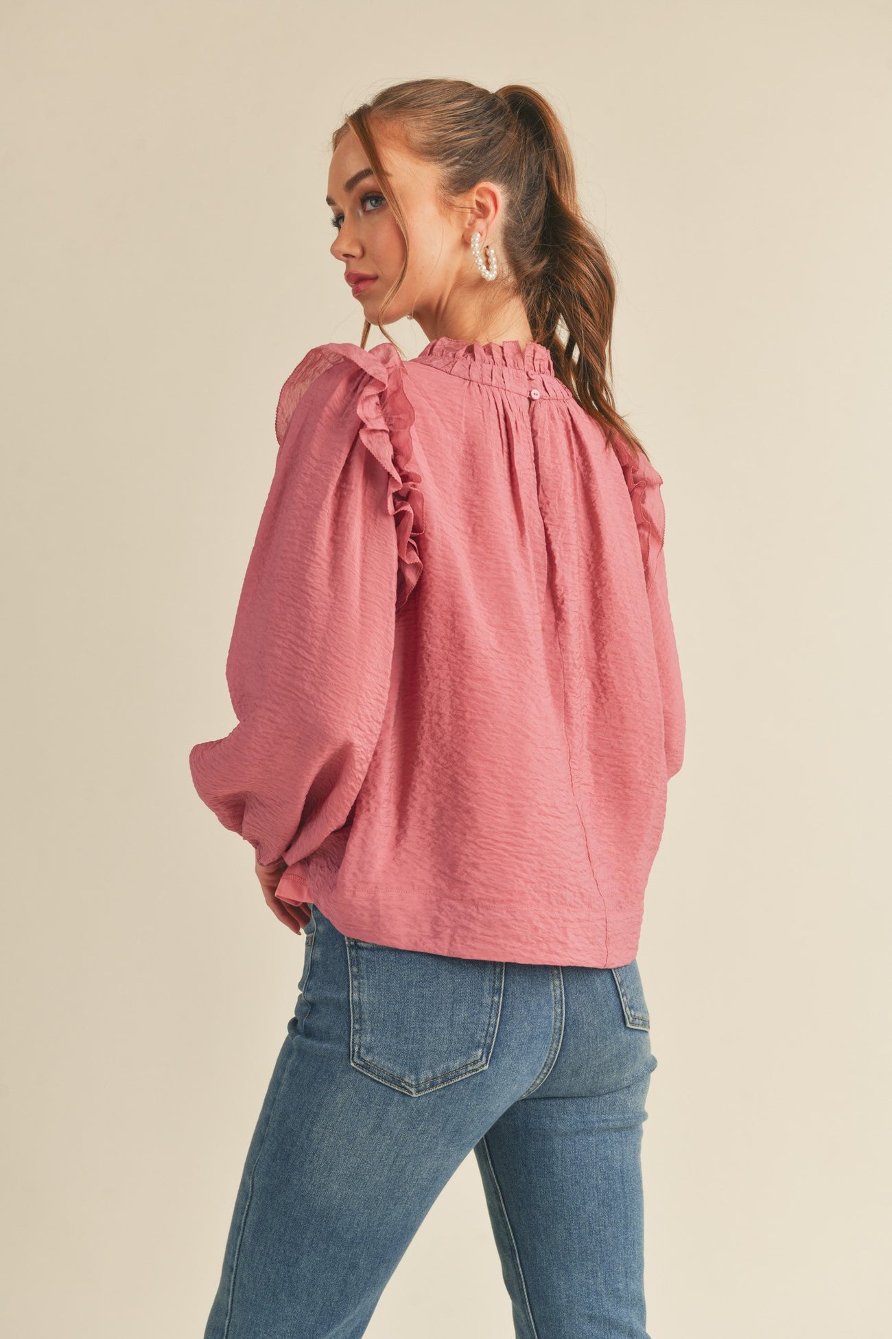 woman wearing a pink ruffled blouse with a loose fit and long sleeves, styled with blue jeans and a ponytail