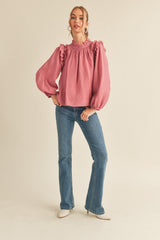 woman wearing a pink ruffled blouse with puff sleeves and blue flared jeans
