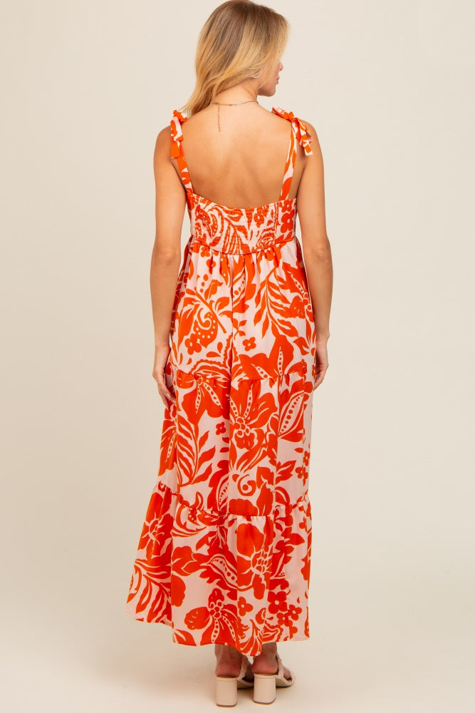 woman wearing a backless orange floral maxi dress with adjustable tie straps, showing a fitted bodice and flowing skirt