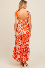 woman wearing a backless orange floral maxi dress with adjustable tie straps, showing a fitted bodice and flowing skirt