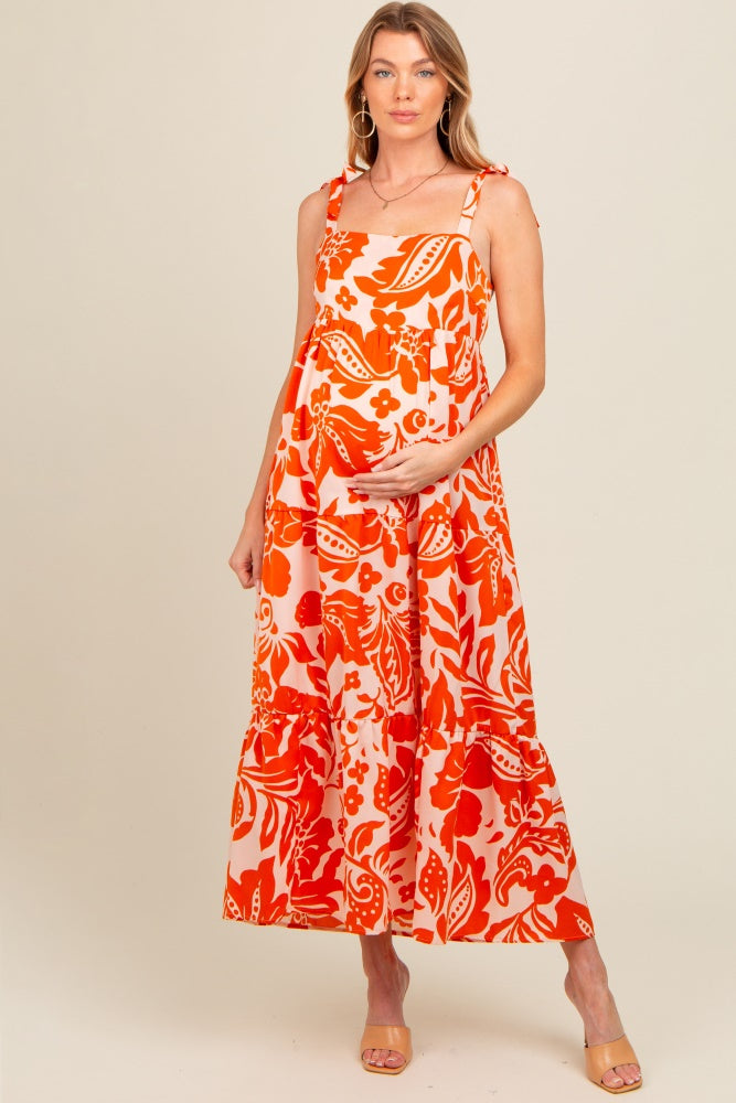 woman wearing a pink and orange floral maternity maxi dress with tied straps and a visible baby bump