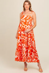 woman wearing a pink and orange floral maternity maxi dress with tied straps and a visible baby bump