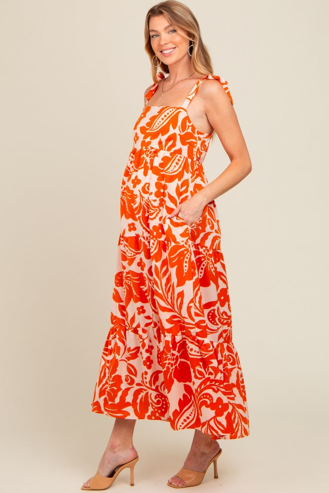 woman wearing an orange floral maternity maxi dress with ruffled straps and pockets, showing a baby bump