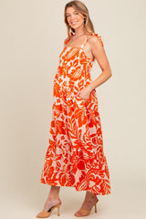 woman wearing an orange floral maternity maxi dress with ruffled straps and pockets, showing a baby bump