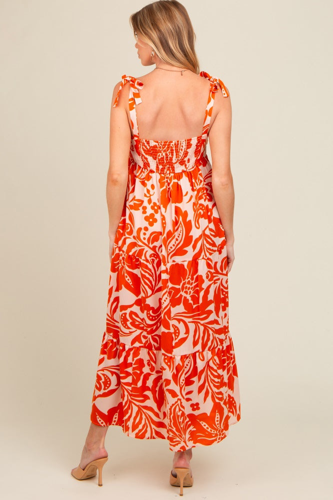 woman wearing a red and orange floral print maternity maxi dress with tie straps, showing the back design