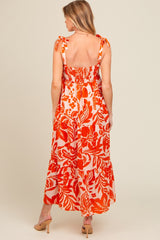 woman wearing a red and orange floral print maternity maxi dress with tie straps, showing the back design