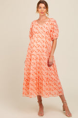 woman wearing a coral floral maternity dress with puff sleeves and a flowing skirt, showcasing her baby bump