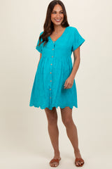 woman wearing a turquoise short sleeve maternity dress with button front and scalloped hem, showing her baby bump