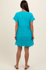 woman wearing a turquoise short sleeve maternity dress with scalloped hem, showing a relaxed fit.