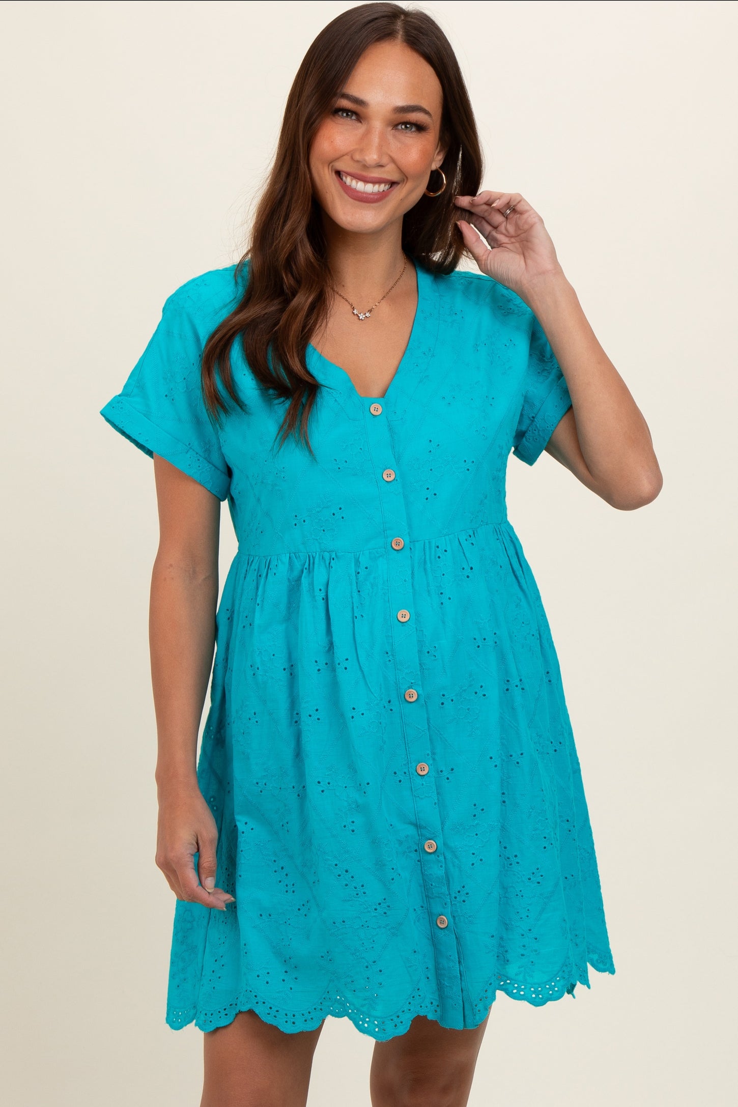 woman wearing a turquoise maternity dress with short sleeves, buttons down the front, and eyelet details