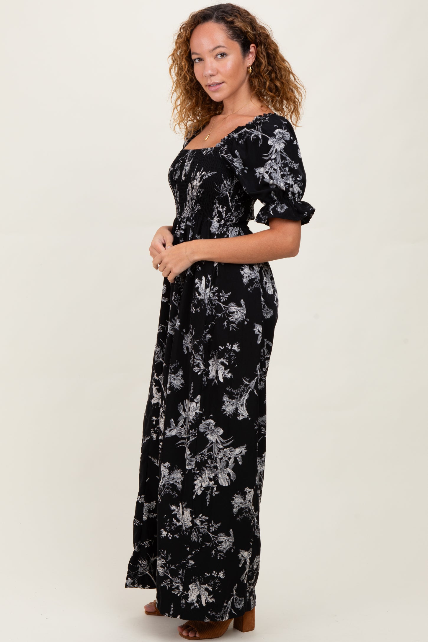 woman wearing a black floral maxi dress with puff sleeves and a fitted bodice, standing sideways against a light background