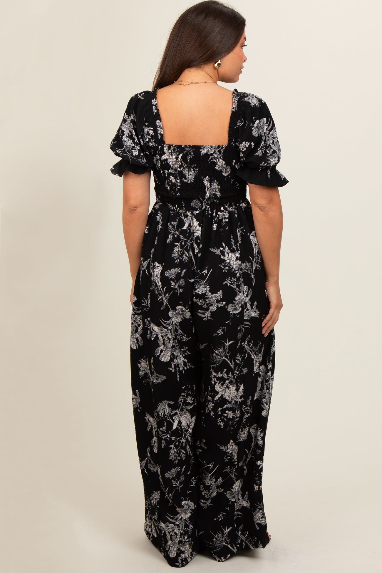 woman wearing a black floral maternity maxi dress with puff sleeves and smocked bodice, showing the back view