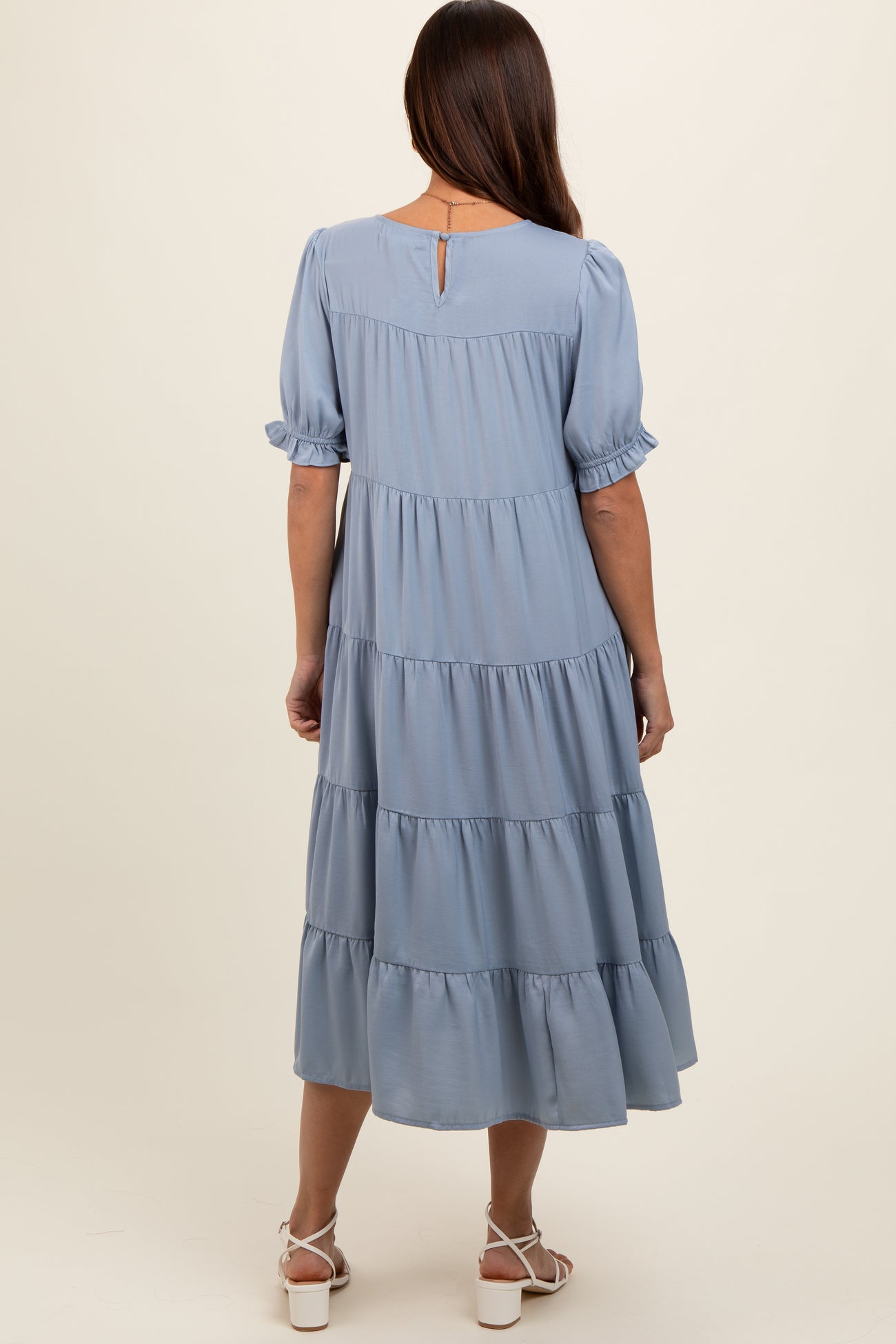 woman wearing a light blue tiered maternity dress with short puff sleeves and a keyhole back detail