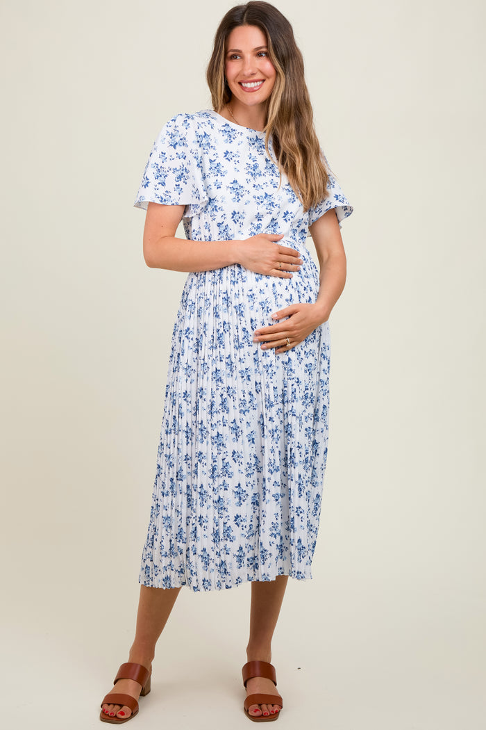 woman wearing a white floral maternity dress with short sleeves and a pleated skirt, holding her baby bump
