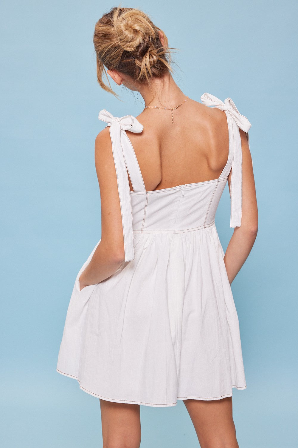 woman wearing a white sleeveless dress with tie straps and a flared skirt, shown from the back