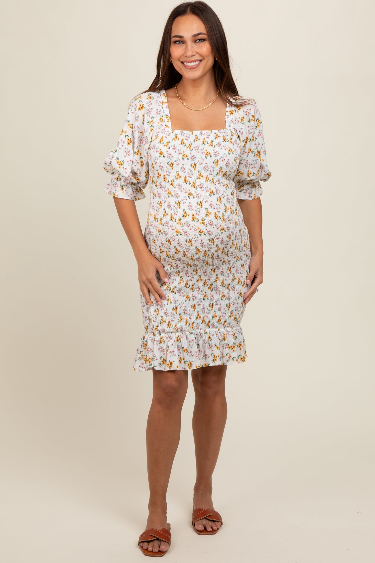 woman wearing a white floral maternity dress with puff sleeves and ruffle hem, showcasing her baby bump