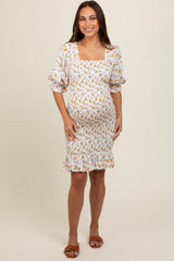 woman wearing a white floral maternity dress with puff sleeves and ruffle hem, showcasing her baby bump