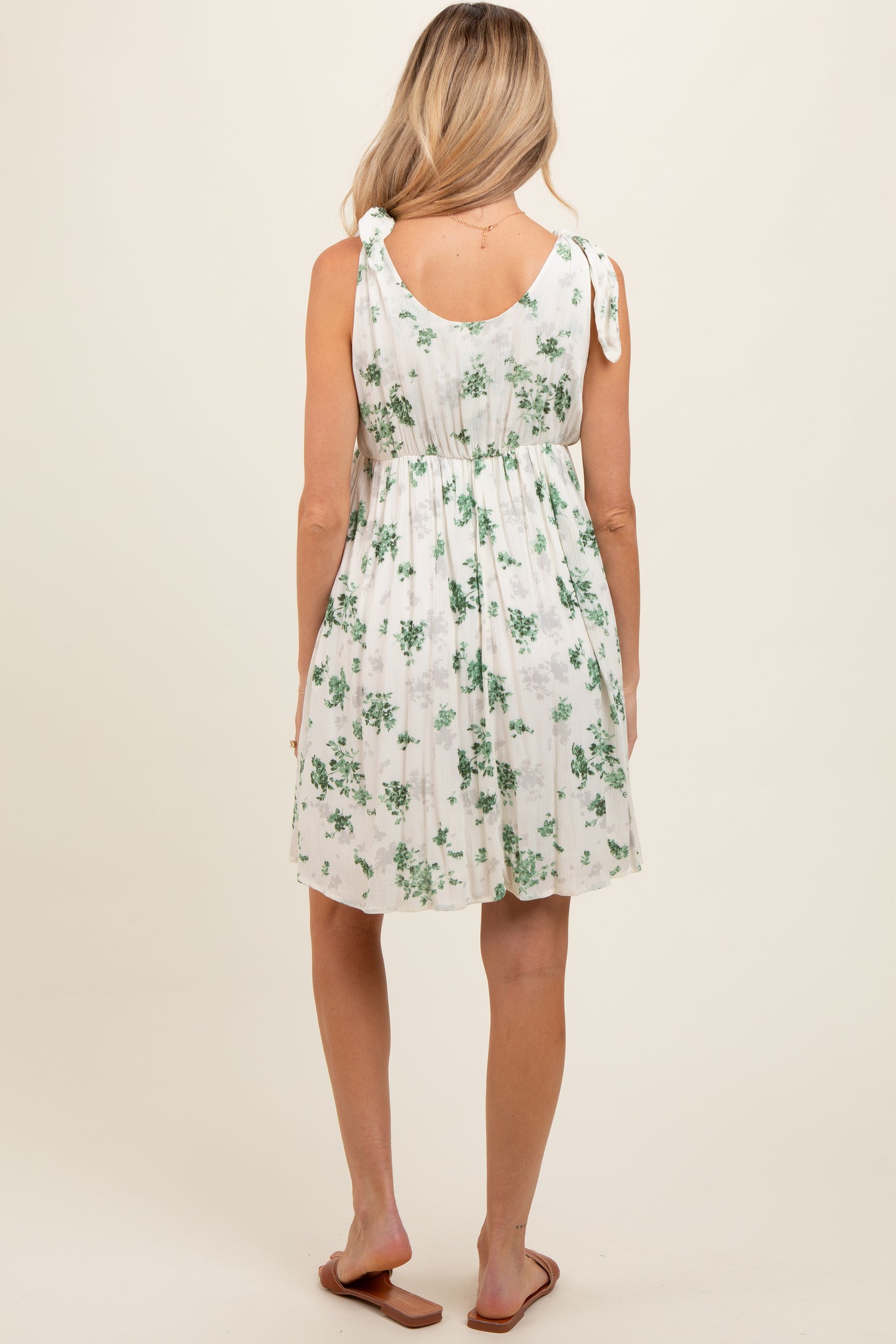 woman wearing a white floral maternity dress with adjustable tie straps and a gathered waist, showing a baby bump