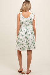woman wearing a white floral maternity dress with adjustable tie straps and a gathered waist, showing a baby bump