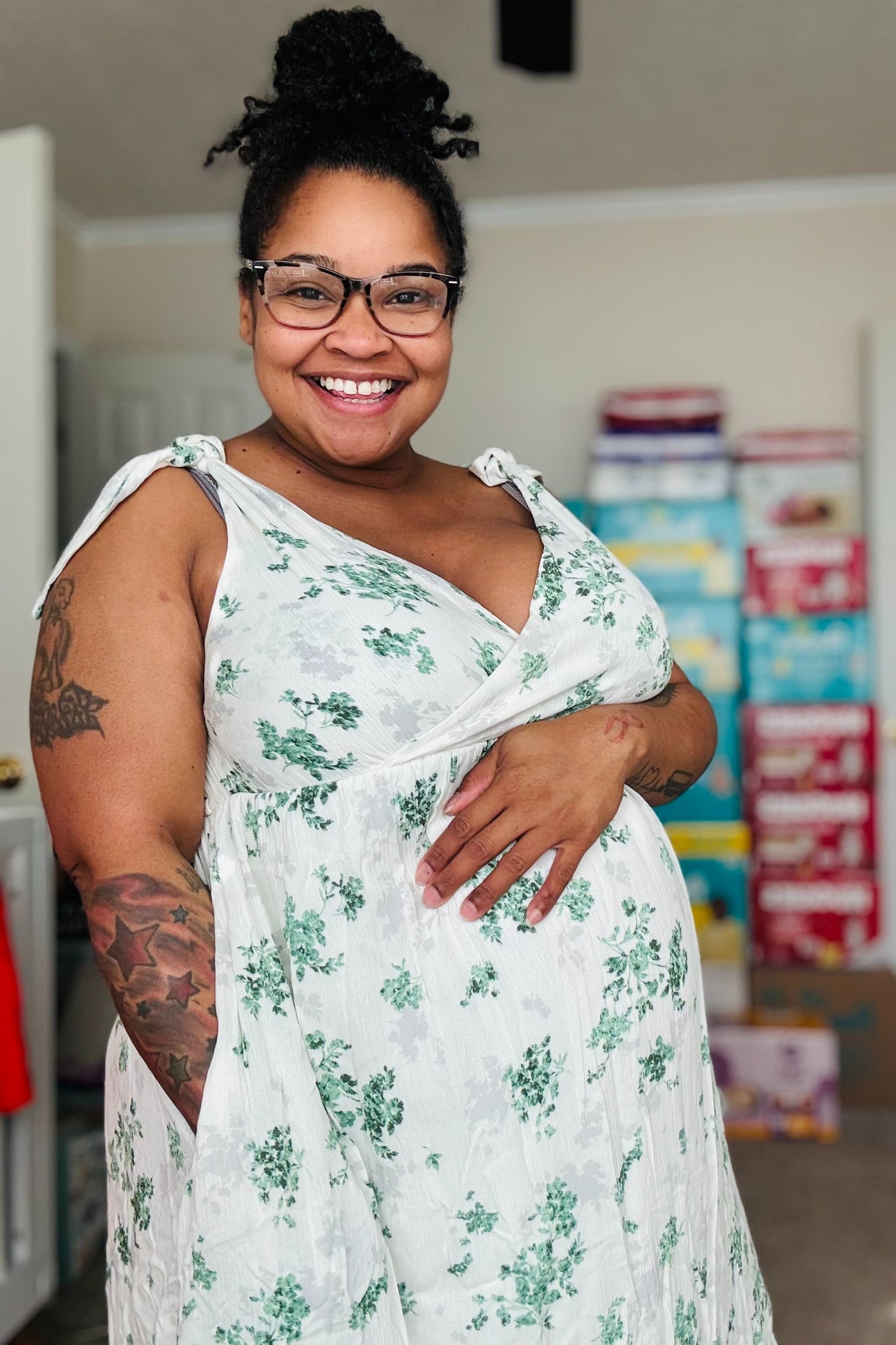 woman wearing a white floral maternity dress with tie straps and holding her baby bump