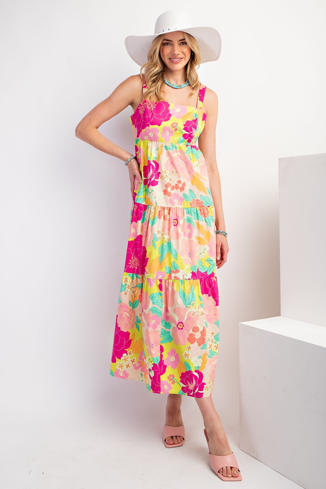 woman wearing a floral maxi dress in pink, yellow, and green with tiered ruffles and a wide-brimmed hat