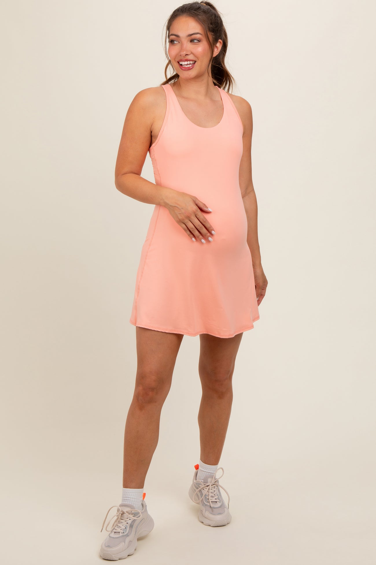 woman wearing a light pink maternity active dress, showcasing her baby bump, paired with sneakers