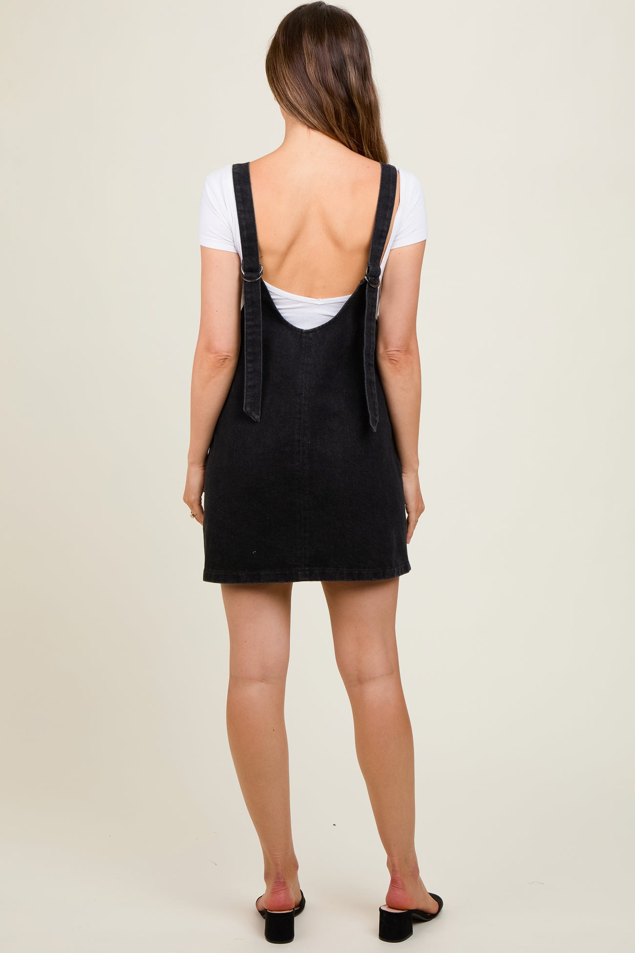 woman wearing a black denim dungaree dress over a white top, maternity wear, back view