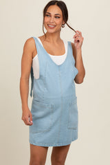 woman wearing a light blue maternity denim dress with pockets and a white tank top, showing a baby bump