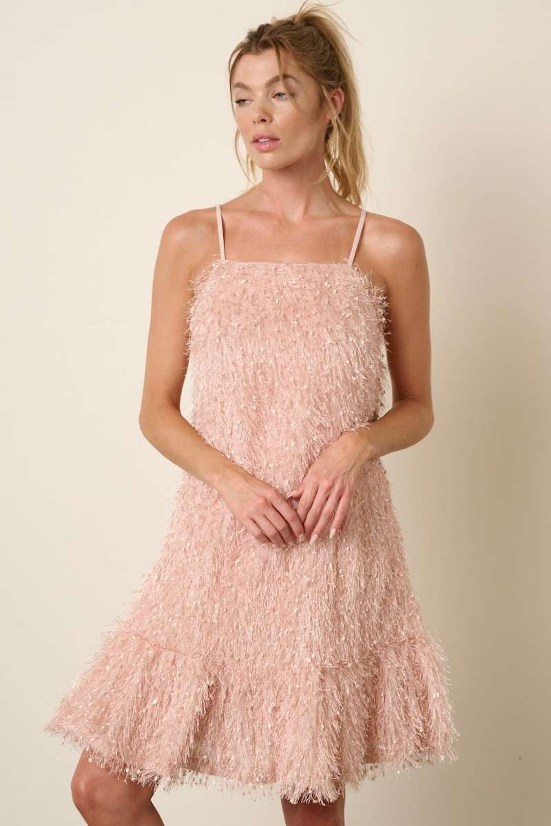 woman wearing a blush pink spaghetti strap dress with fringe detailing and a flared hem