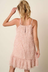 woman wearing a light pink fringe dress with a tiered hem and adjustable straps, viewed from the back