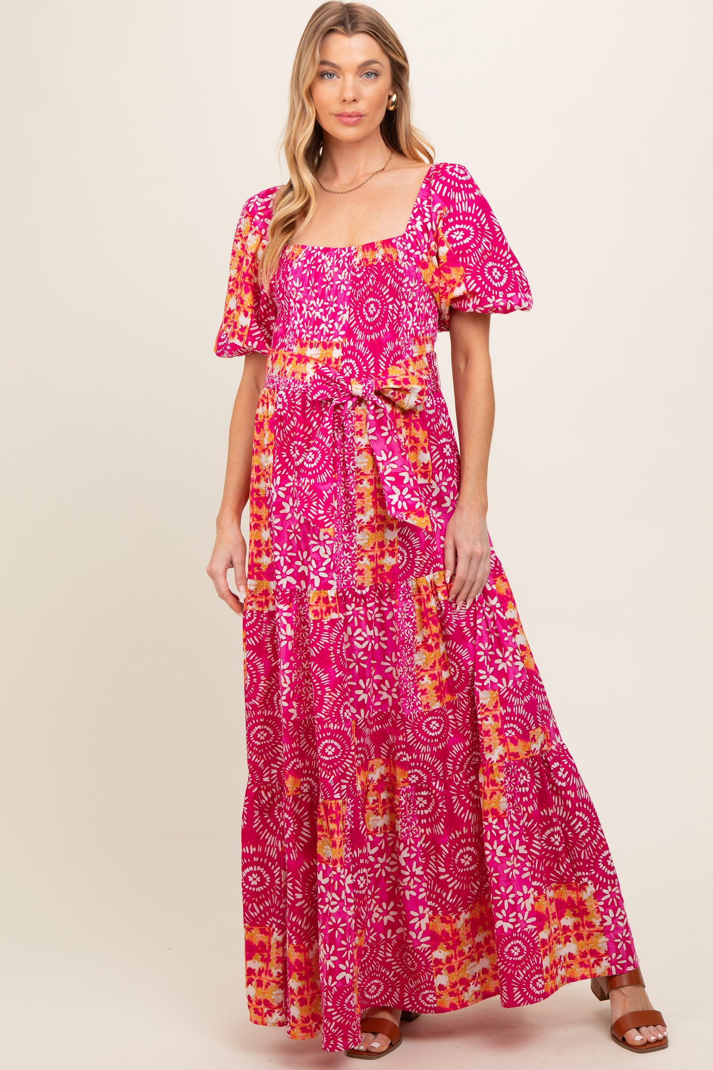 woman wearing a pink floral maternity maxi dress with puff sleeves and a tie waist, showcasing her baby bump