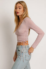 woman wearing a light pink long sleeve cropped top with side ruching and paired with light blue high-waisted jeans