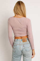 woman wearing a light pink long sleeve top with a ruched back, paired with high-waisted blue jeans
