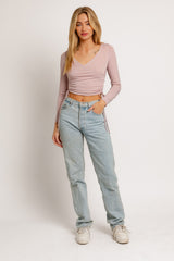woman wearing a light pink long sleeve wrap top and light blue high-waisted jeans, standing against a white background