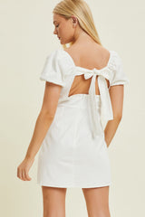 woman wearing a white short dress with puff sleeves and a back tie detail