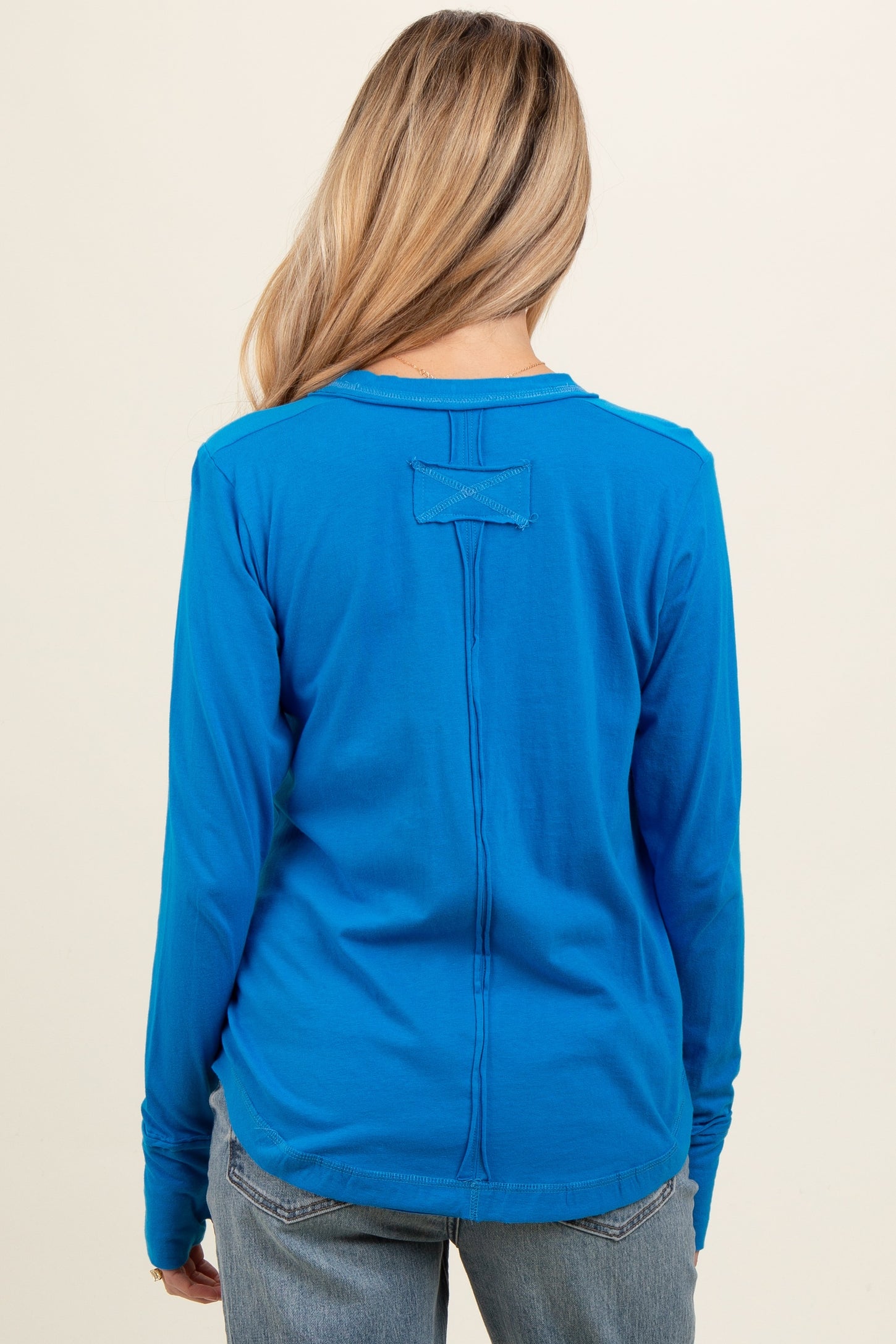 woman wearing a vibrant blue long sleeve maternity top, showing the back view with a simple design detail