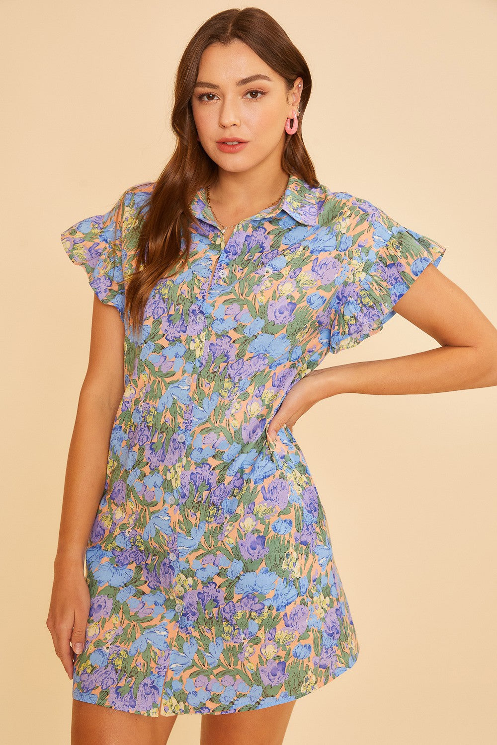 woman wearing a short sleeve floral button-up dress in blue, purple, and green with ruffled sleeves
