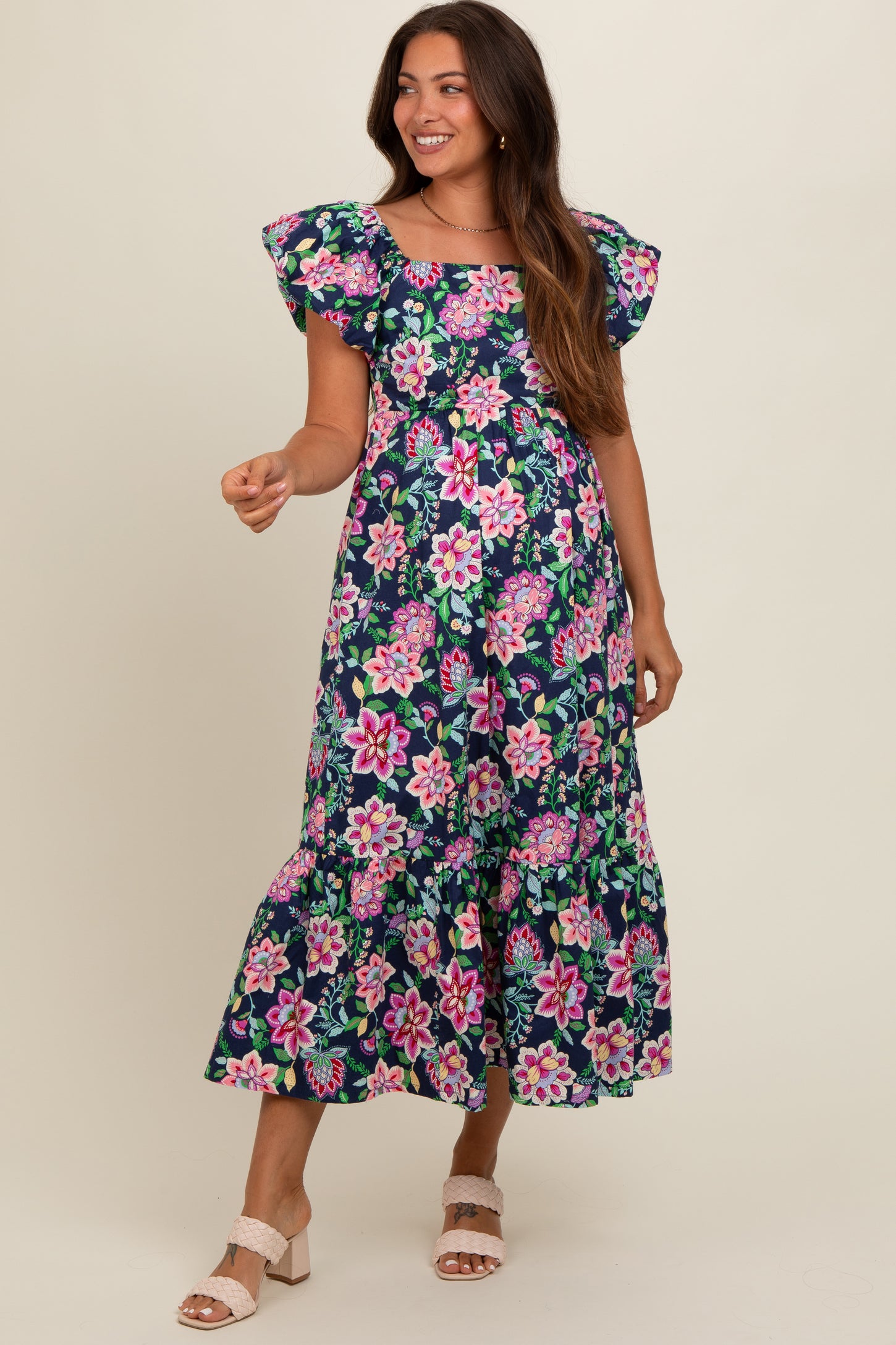 woman wearing a navy floral maternity maxi dress with ruffle sleeves and a tiered skirt, smiling while posing