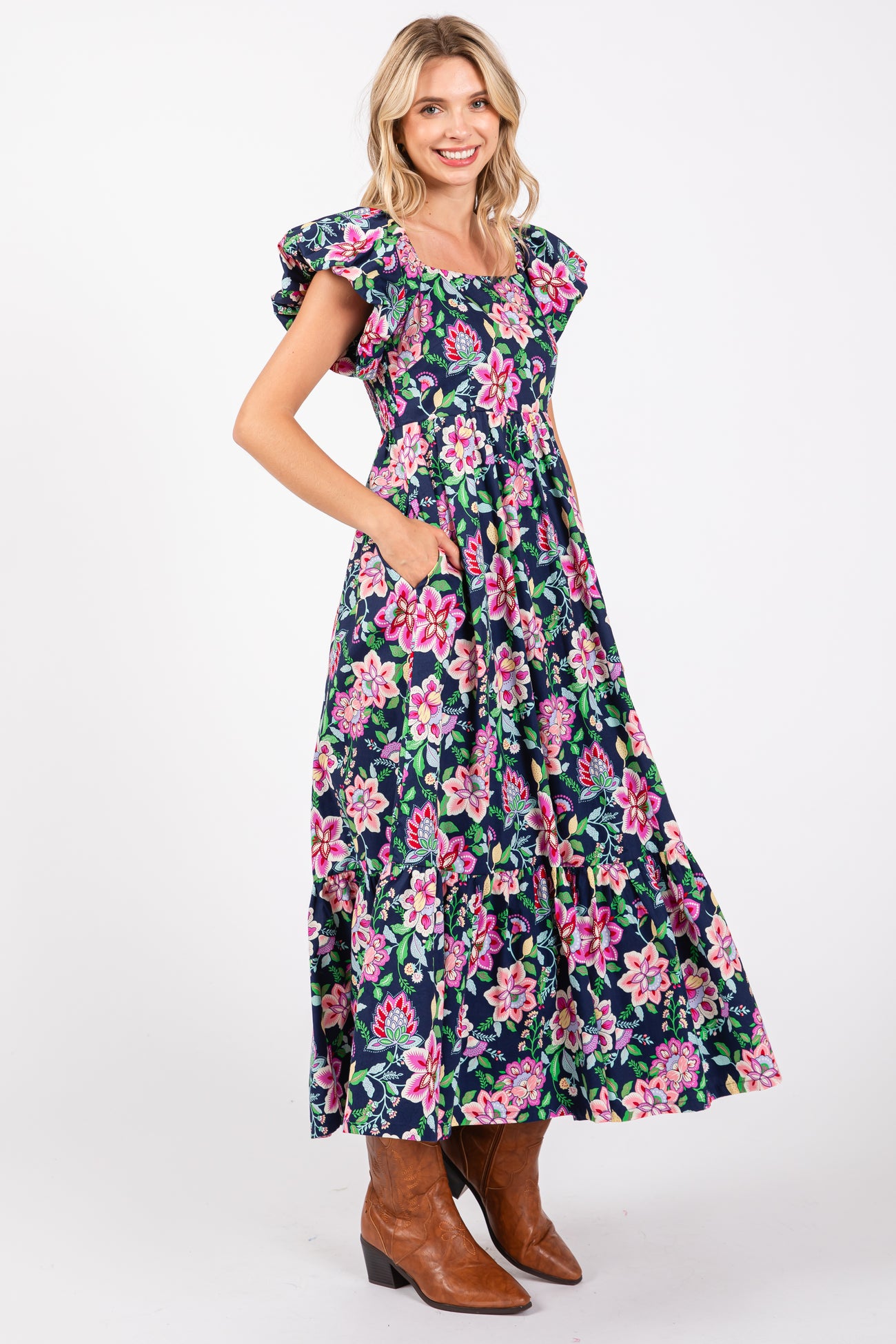 woman wearing a floral maxi dress with ruffled sleeves and pockets, paired with brown cowboy boots