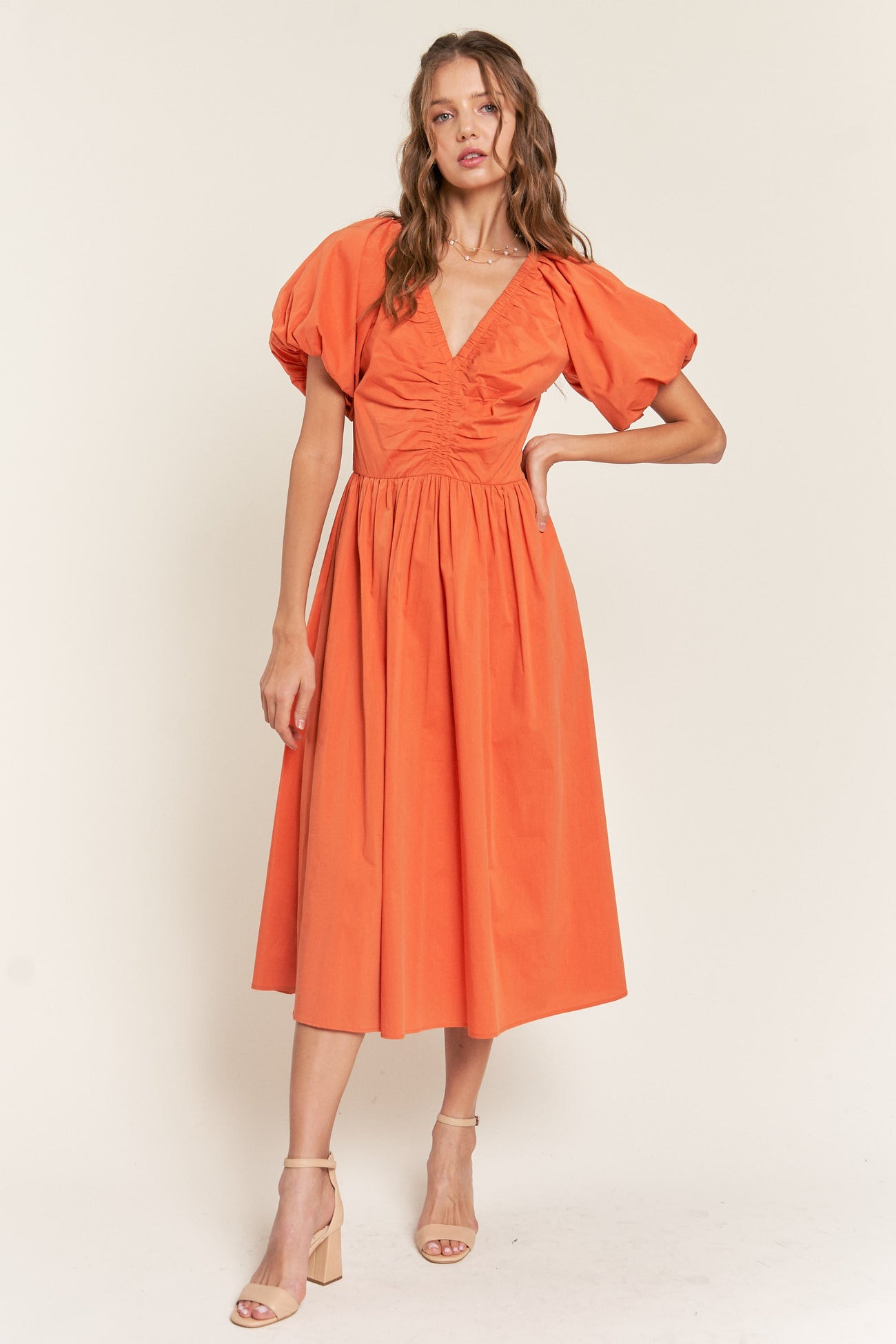 woman wearing an orange puff sleeve midi dress with a v-neck and gathered detailing