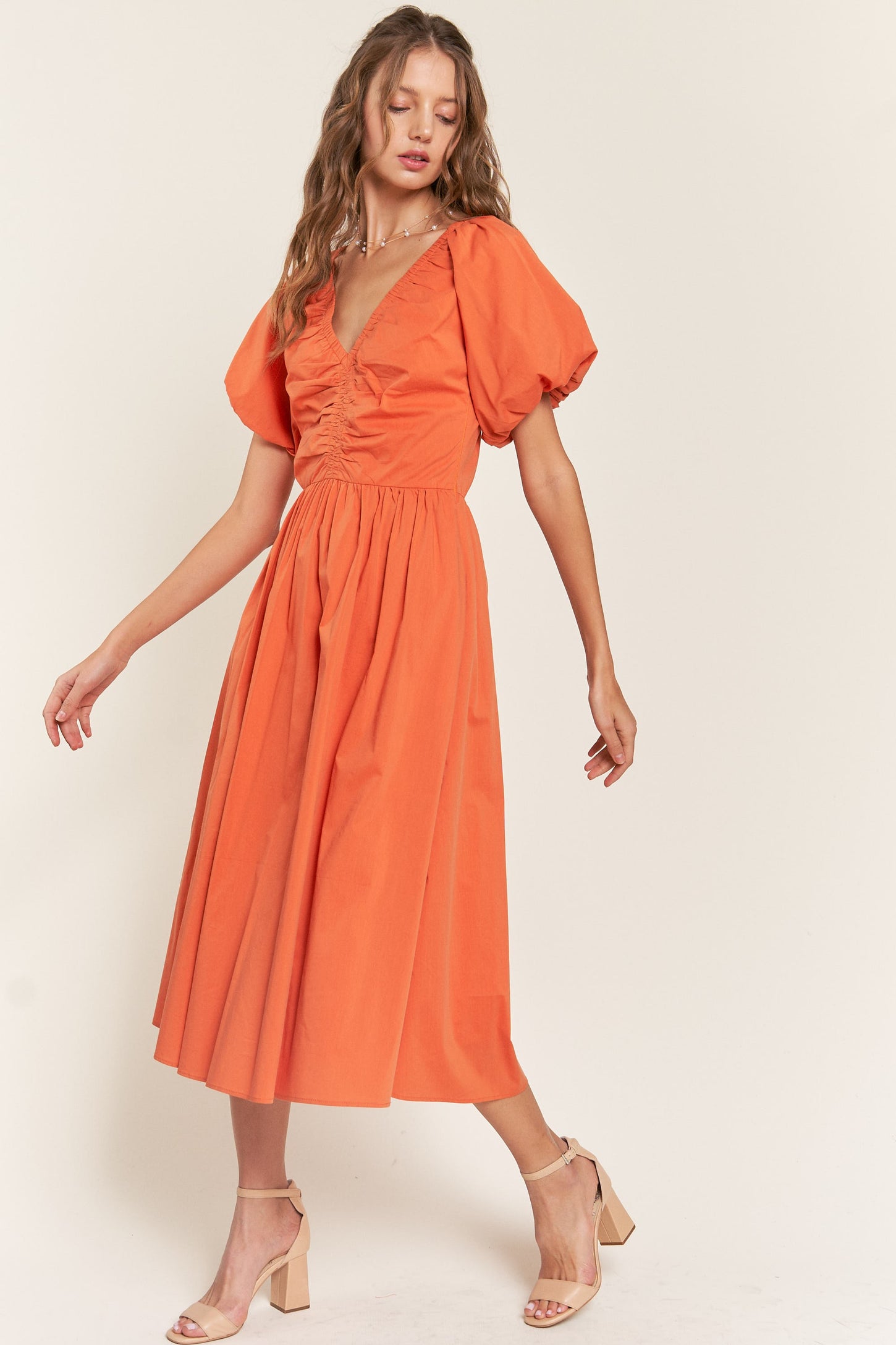woman wearing an orange midi dress with puff sleeves and a cinched waist, styled with strappy heels