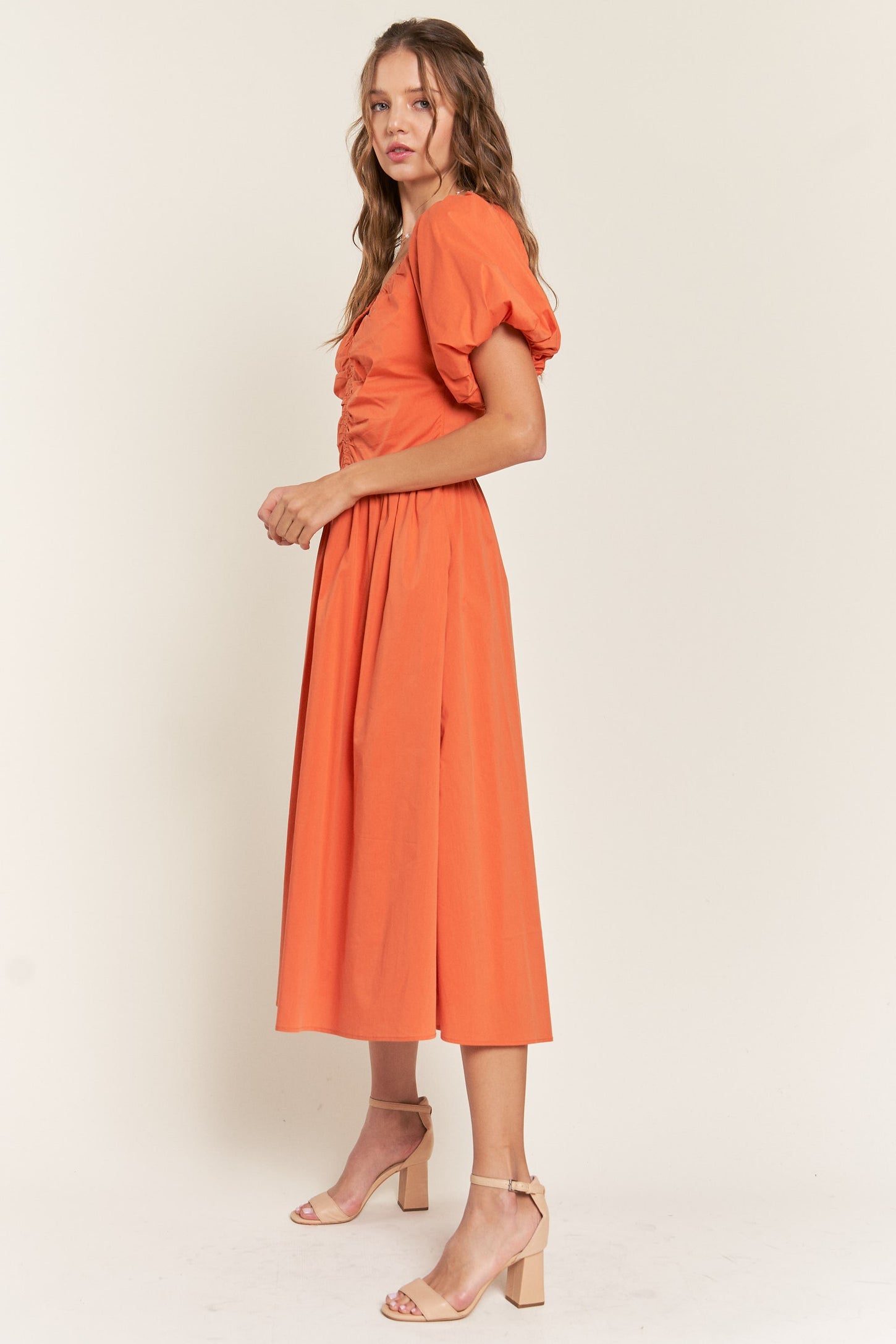 woman wearing an orange puff sleeve midi dress with a fitted bodice and flared skirt